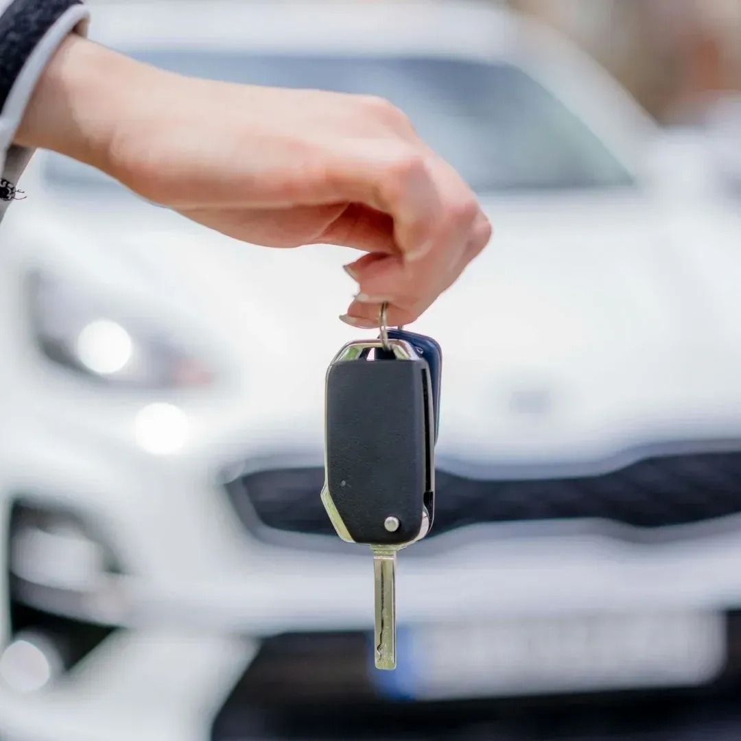 Hand holding a car key fob in front of a blurred white car